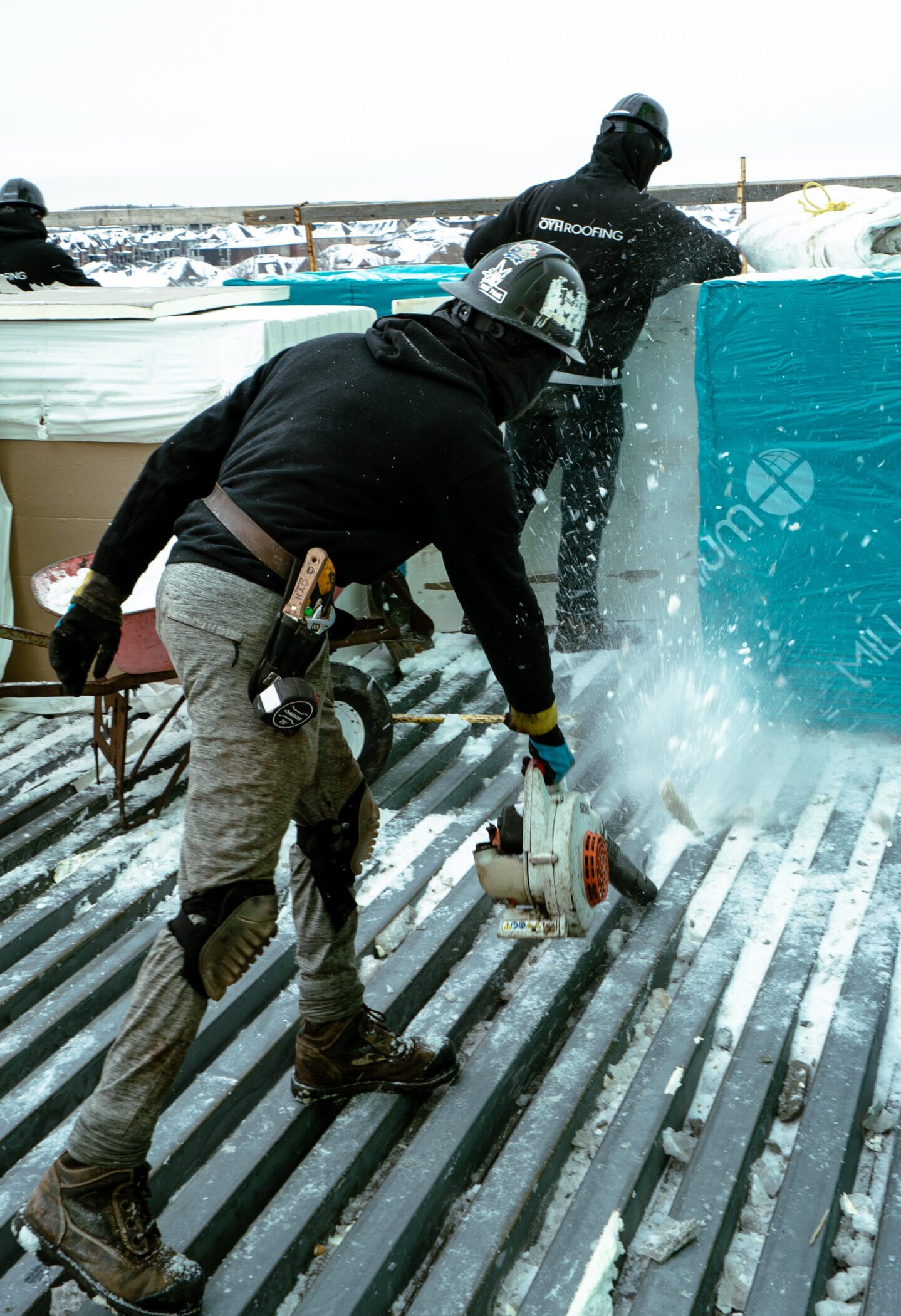 Modified bitumen roof installation in winter: an OYH Roofing crew clears snow and ice from a steel deck before the roof goes on