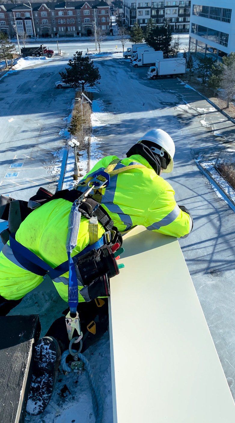 Fall protection for commercial roof drainage repair at the roof edge: an OYH Roofing worker in a full-body harness and lifeline in winter